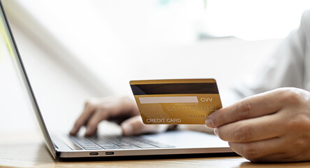 A guy holds a credit card and is filling out his credit card information on his laptop to place an order on the website. Credit cards can be used to pay for goods or services with online merchants.