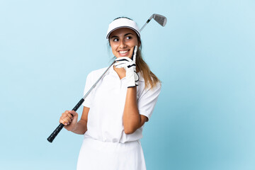 Young hispanic golfer woman over isolated blue wall thinking an idea while looking up