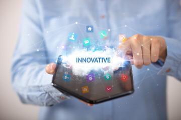 Businessman holding a foldable smartphone with INNOVATIVE inscription, technology concept