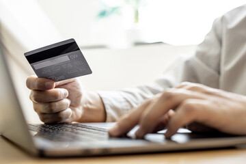 Man holding a credit card and filling out his credit card information on his laptop. Credit cards can be paid for goods and services through general merchants or online stores. Credit card concept.