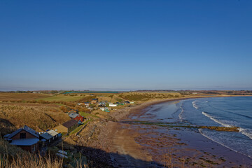 Obraz premium The small community of Korbie Knowe sheltered below the Cliffs at the southern end of lunan Bay facing the sandy beach with the tide going out.