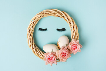 Easter wreath with false eye lashes and easter eggs, flowers pink roses on blue background