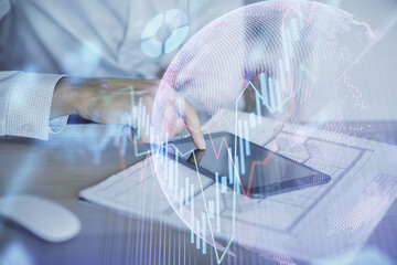 Double exposure of man's hands holding and using a digital device and forex graph drawing. Financial market concept.