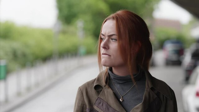 [4k] A young an beautiful but sad ginger woman standing on a car park is pouting while biting her lips and nodding her head