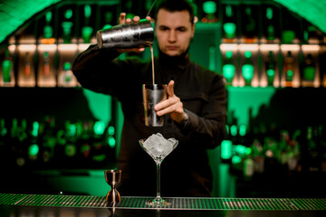 martini glass with ice and jigger stands on bar. Blurred bartender in background