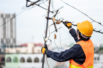 Male electrical worker or Asian man electrician wearing safety helmet and reflective suit repairing an old TV antenna and cable on rooftop of building.