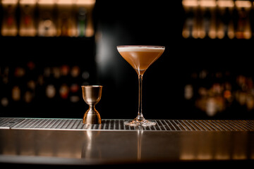 beautiful view of martini glass with cocktail and jigger standing on bar counter.