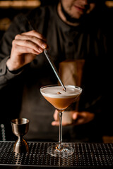 beautiful view on glass with frothy cocktail which bartender decorates with coffee bean using tweezers