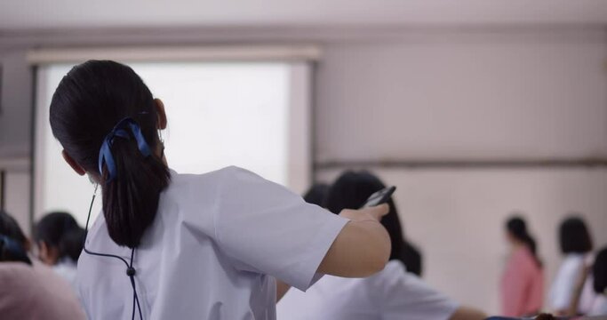 An Asian female student in a white school uniform and wearing a mask to prevent covid-19, sitting in study group using a calculator to solve problems by teachers with a projector.