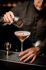 bartender gently sprinkles colored powder on foam of espresso martini cocktail in glass