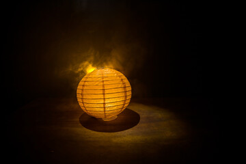 Beautiful paper lantern glowing on wooden table in dark.