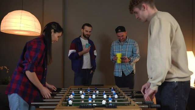 Group of young people having fun playing in kicker at Home Party. Drinking beer