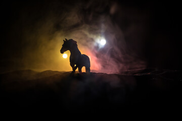 Beautiful horse running in desert at night. Silhouette of a horse miniature standing at foggy night. Creative table decoration with colorful backlight with fog. Selective focus