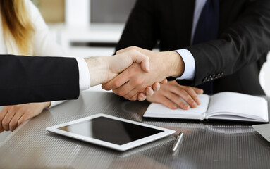 Unknown businessmen shaking hands above the glass desk in a modern office, close-up. Unknown business people at meeting. Teamwork, partnership and handshake concept