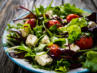 Fresh vegetable salad with feta cheese, tomatoes, arugula, lettuce and roast tomatoes on wooden...