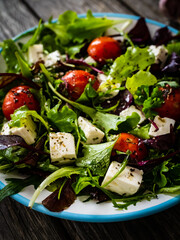 Fresh vegetable salad with feta cheese, tomatoes, arugula, lettuce and roast tomatoes on wooden table
