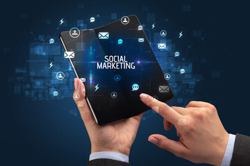 Businessman holding a foldable smartphone with SOCIAL MARKETING inscription, social networking concept