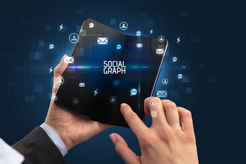 Businessman holding a foldable smartphone with SOCIAL GRAPH inscription, social networking concept