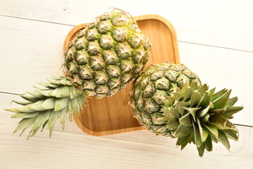 Two organic juicy pineapples with a plate of bamboo on a wooden table, close-up, top view.