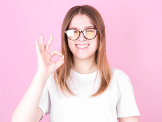 Cheerful funny cute girl gesturing ok on the pink background