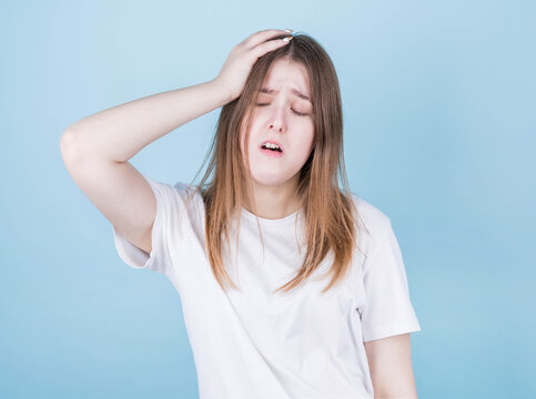 Portrait of a beautiful young brunette woman in a white T-shirt with disheveled hair, holding her head with one ruk, feeling a strong headache, fatigue on a pink background