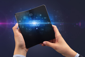Businessman holding a foldable smartphone with HYBRID CLOUD inscription, cyber security concept
