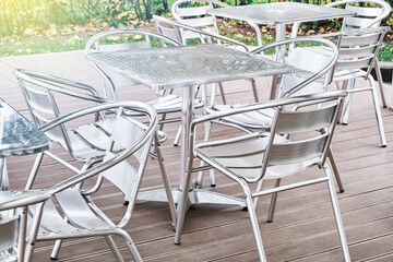 Stylish contemporary empty metallic tables and chairs stand on wooden terrace of summer cafeteria on sunny day close view