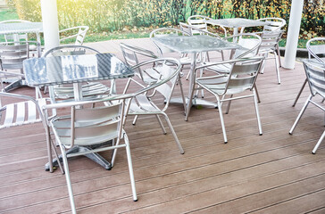 Stylish contemporary empty metallic tables and chairs stand on wooden terrace of summer cafeteria on sunny day close view