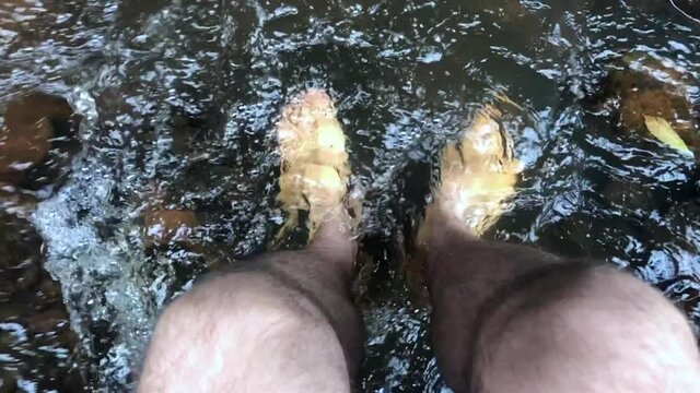 Point of view of a man looking at his feet in the river. Slow motion video.