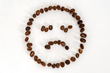 Artificial sad face made from coffee beans on white background. Concept idea, copy space.