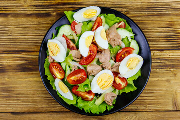 Tasty tuna salad with eggs, lettuce and fresh vegetables on wooden table. Top view