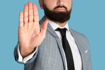 Cropped view of millennial businessman refusing something, showing STOP gesture on blue studio background