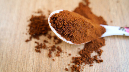 Coffee powder in the Spoon isolated on table wooden background. Pile of brown coffee spilling on ground, Indian spices