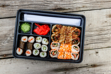 Set of sushi rolls in plastic box on wooden table. Sushi for take away or delivery of sushi in plastic container. Top view