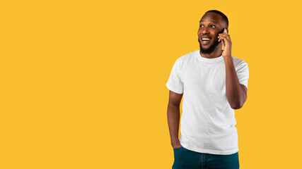 Black Man Talking On Cellphone Looking Aside Over Yellow Background