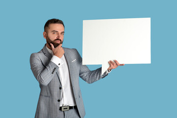 Thoughtful young entrepreneur holding empty speech bubble on blue studio background, mockup for design