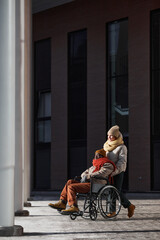 Vertical wide angle view at African American man in wheelchair moving in urban city lit by sunlight...