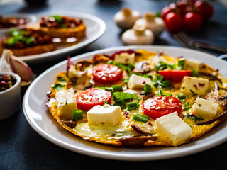 Delicious breakfast - scrambled eggs with onion, feta cheese, cherry tomatoes, champignons and chives on wooden table
