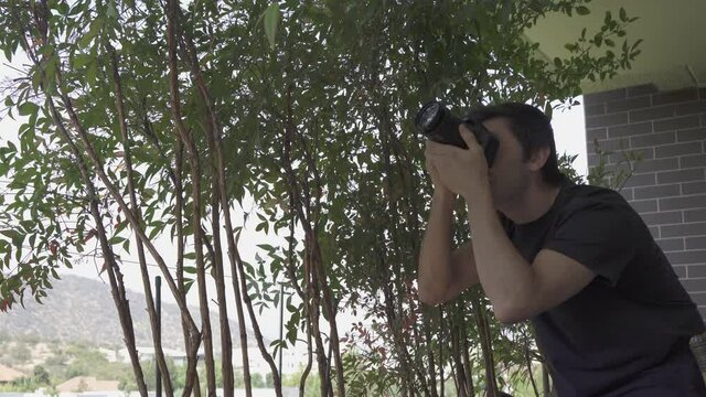Young man taking pictures of trees with dslr camera. Photographer looking for best angle at home terrace