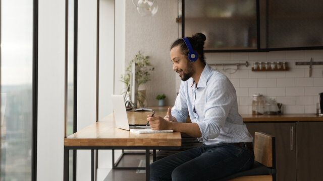 Side View African American Man Wearing Headphones Writing, Taking Notes, Using Laptop, Motivated Student Watching Webinar, Listening To Lecture, Studying Online At Home, Looking At Computer Screen