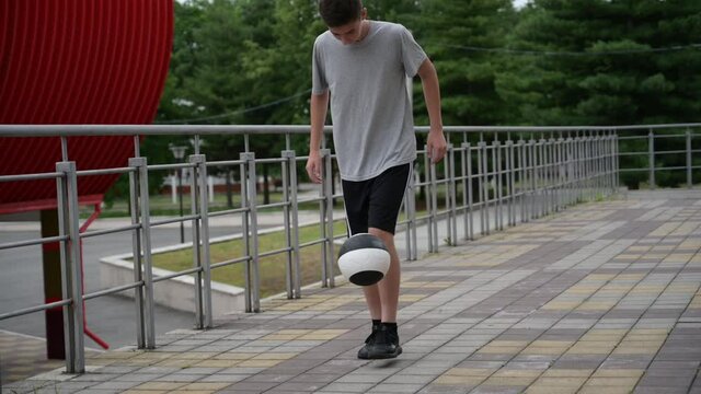 young teen boy juggling ball near city urban football arena in slow motion during keep ups soccer training