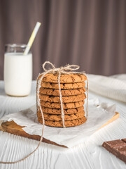 Tied cookies on a stand with a glass of milk, on a white wooden background