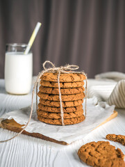 Tied cookies on a stand with a glass of milk, on a white wooden background