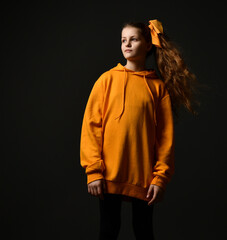 Cute teenage girl with long hair gathered in a ponytail. She poses in a yellow hoodie against a dark studio background.