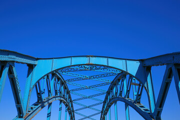 Low angle view on isolated symmetrical industrial steel bridge deck against blue sky with cross struts and metal beams