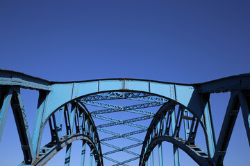 Low angle view on isolated symmetrical industrial steel bridge deck against blue sky with cross struts and metal beams