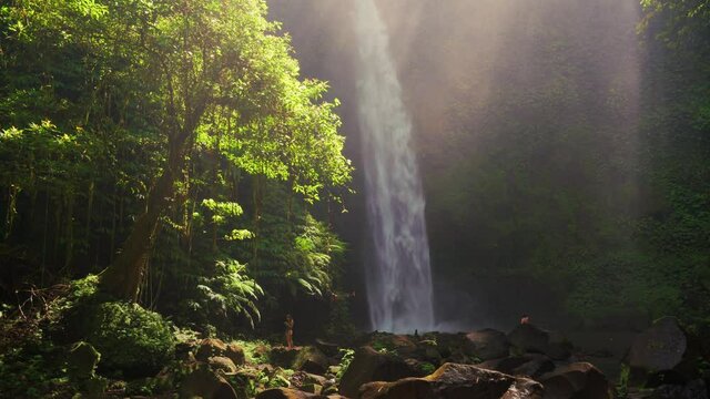 Silhouette travel people enjoying beautiful Waterfall in the rays of the rising sun hidden in tropical rain forest jungle. 4K UHD Video clip