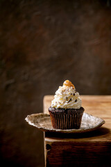 Homemade chocolate cupcakes muffins with white whipped butter cream and salted caramel on ceramic plate, served with chopped dark chocolate on wooden table. Copy space