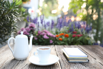 White tea cup and kettle with notebook on wooden table and flower field background