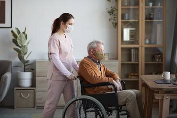 Side view portrait of young female nurse assisting senior man in wheelchair at retirement home,...